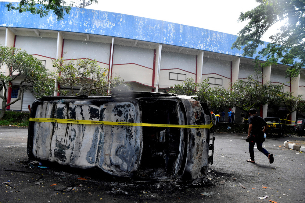 A man walks next to a damaged car following a riot after a football match between Arema vs Persebaya at Kanjuruhan Stadium  / ANTARA FOTO